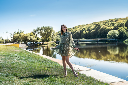 pretty woman in dress was standing by the lake, relax at nature and poses for the camera