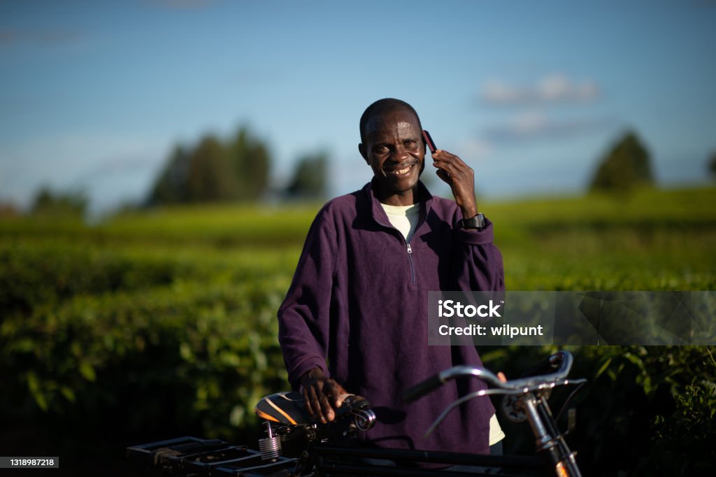 Happy Man with a bicycle looking at camera talking on a mobile phone in a rural setting Happy African Man with a bicycle looking at camera talking on a mobile phone in a rural setting in Southern Malawi Africa African Ethnicity Stock Photo