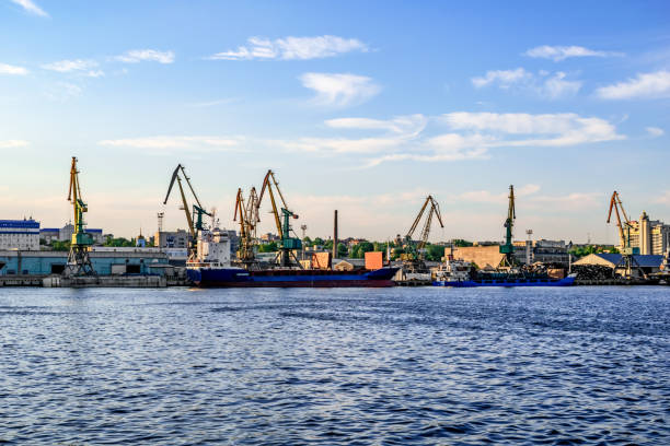 Cargo ships and harbor cranes in the Kherson river port - view from the Dnieper river (Ukraine). Water surface against the background of industrial equipment on the shore