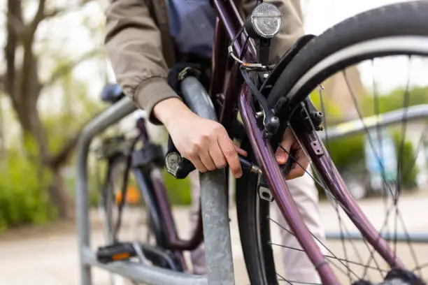 Close-up of a man locking his cycle on the rack in the city. Man locking and securing his bicycle on the sidewalk.