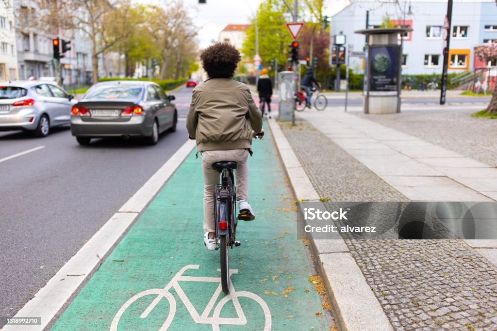 Cyclist in city traffic using the bicycle lane Rear view of a man riding his cycle on green colored bicycle lane. Male cyclist commuting in city traffic. Cycling Stock Photo