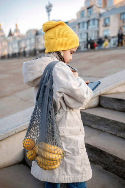 preteen chica sentada en las escaleras de la calle y enviando mensajes de texto con el teléfono inteligente en el camino de las compras - artists canvas yellow white red fotografías e imágenes de stock