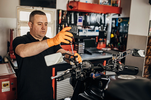 One man, male motorcycle mechanic repairing motorcycle in his workshop.