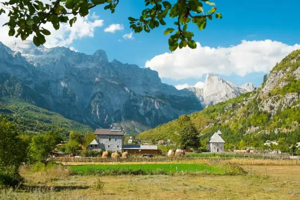 Beautiful view of the small and historic village of Theth with church and the surrounding mountains with green trees. Sunny late summer weather with blue sky. Theth National Park, Albania.