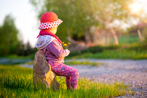Little girl with flowers in hand sits on the stone