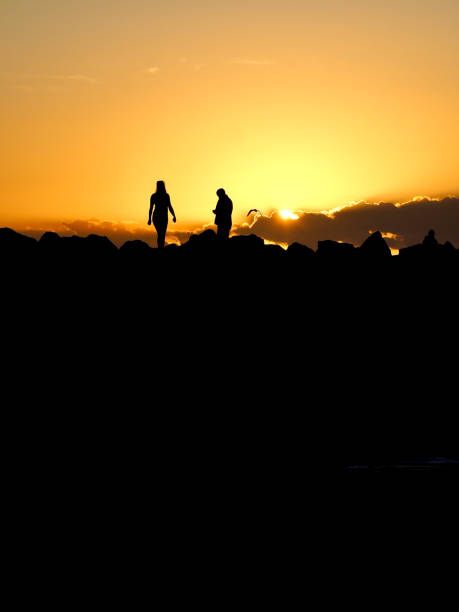Sunrise at Brunswick Heads, NSW Vertical photo of two people and the rock wall in silhouette against the gold and orange sky at sunrise on the sub tropical north coast of NSW near Byron Bay. brunswick heads nsw stock pictures, royalty-free photos & images