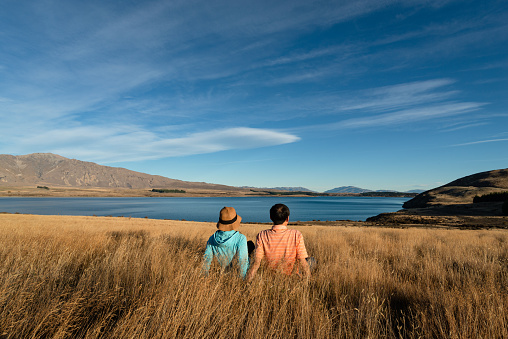 Couple sitting on the long grass and enjoying views of Lake Tekapo from Peninsula walkway, South Island