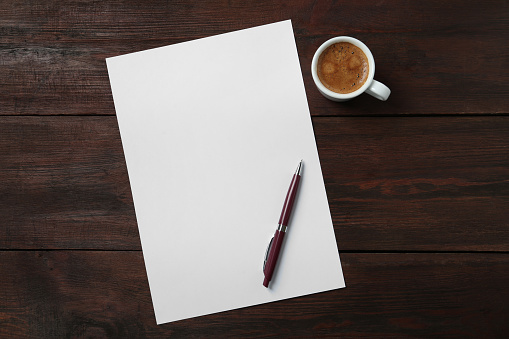 Blank paper sheet, pen and cup of coffee on dark wooden table, flat lay. Space for text