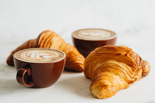 Stilllife of two cups of cappuccino and two croissant on white table