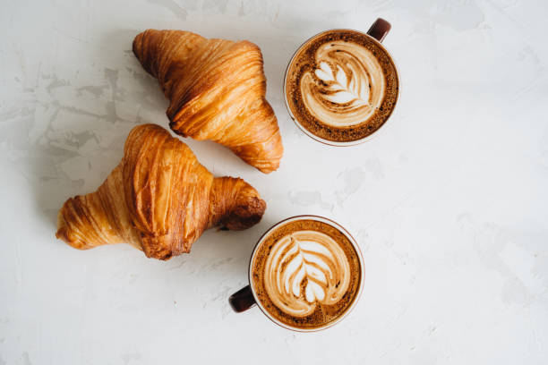 istock Two cups of coffee and croissant on white table 1318999776