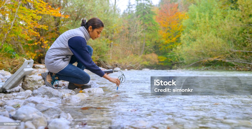 Female biologist testing the oxygen levels in the river Side view of young female biologist using multiparameter instrument while testing dissolved oxygen in river. Water Stock Photo