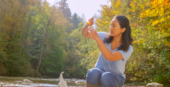 Female biologist adding reagent into a vial with water sample near river.