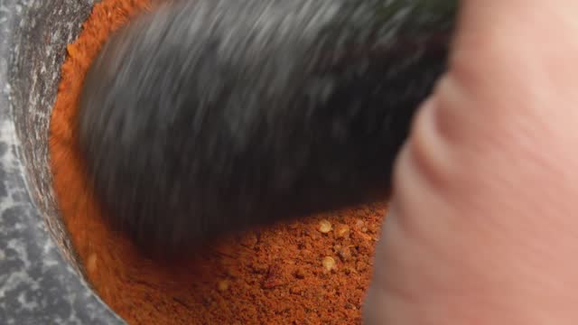 Close-up of the pestle mixing spices and peppers in the stone mortar