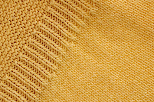 Close-up texture of handmade knitted woolen fabric in beige, ivory, cream color. Textile background, top view, copy space