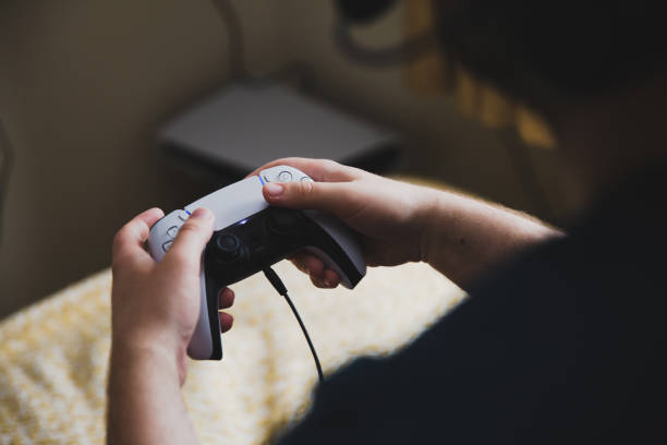 Close up of a pair of hands holding a PlayStation 5 video game controller York, UK - May 9, 2021.  Close up of a teenage boy holding a PS5 gaming console controller whilst playing video games brand name games console stock pictures, royalty-free photos & images