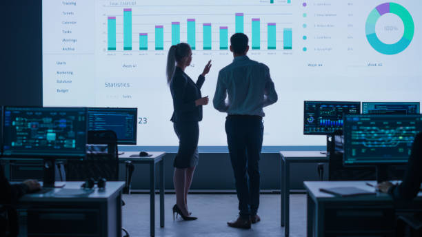 Project Leader, Chief Executive Discuss Data Shown on Big Display. Screens Show Infographics, Charts, Finance Analysis, Stock Market, Growth.Telecommunications Control Room with Working Professionals líder del proyecto, director ejecutivo discute los datos mostrados en big display. pantallas muestran infografías, gráficos, análisis financiero, mercado de valores, crecimiento.sala de control de telecomunicaciones con profesionales en funcionamiento