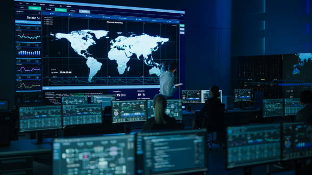istock Project Manager Uses Digital Tablet Looks at Big Screen Display Showing Infographics and Global World Map Data. Telecommunications Control Monitoring Room with People Working 1319010442