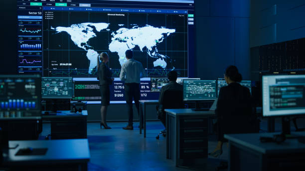 istock Project Manager Uses Digital Tablet Talks with Computer Scientist Looks at Big Screen Display Showing Infographics Global World Map Data. Telecommunications Control Control Room with People Working 1319010444