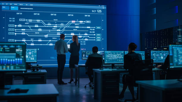 istock Telecommunications Company System Control and Monitoring Room with Diverse Multicultural Team of Professionals Working on Computers. Big Screen Display Showing Infrastructure Infographics. Back View 1319010512