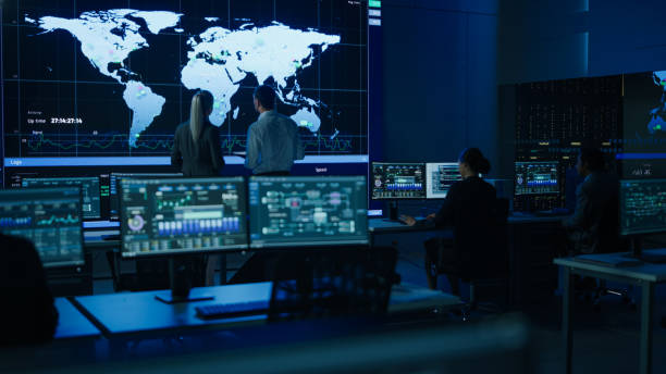 istock Project Manager Uses Digital Tablet Talks with Computer Scientist Looks at Big Screen Display Showing Infographics Global World Map Data. Telecommunications Control Control Room with People Working 1319010528