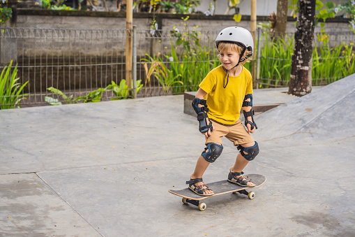 Athletic boy in helmet and knee pads learns to skateboard with in a skate park. Children education sports.