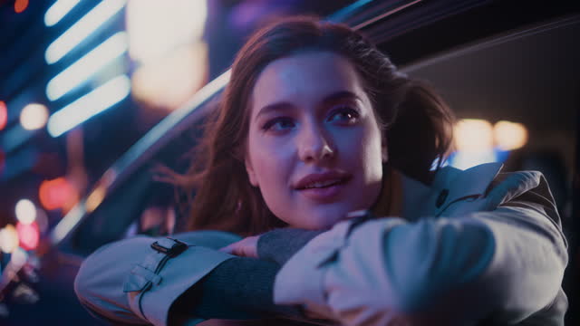 Excited Young Female is Sitting on Backseat of a Car, Commuting Home at Night. Looking Out of the Window with Amazement of How Beautiful is the City Street with Working Neon Signs. Cinematic Footage.