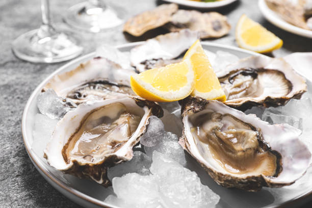 灰色のテーブルにレモンと氷を入れた新鮮な牡蠣、クローズアップ - prepared oysters ストックフ�ォトと画像