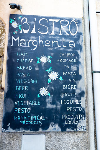 Corniglia, La Spezia-Italy - 27.08.2020: A black board of a bistro, on which various foods and drinks are written in turquoise and white letters, everything is decorated with flowers.