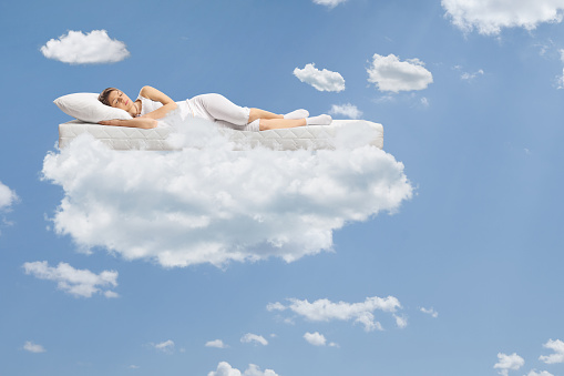 Young woman sleeping on a floating mattress up in the clouds and a blue sky