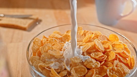 Close-up of milk pouring into a bowl of cornflakes on table.
