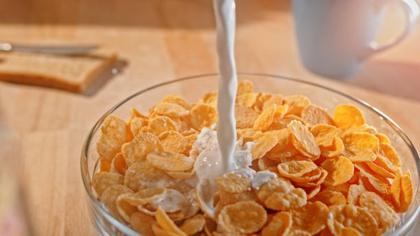 Milk pouring into a bowl of cornflakes Close-up of milk pouring into a bowl of cornflakes on table. cornflakes stock pictures, royalty-free photos & images