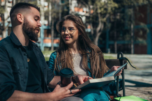 istock Two students sitting on a bench in a campus and studying for their exam 1319014667
