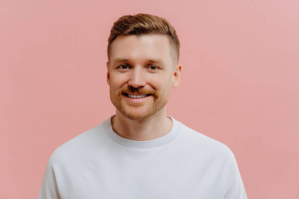 Young positive man smiling at camera in pink studio background