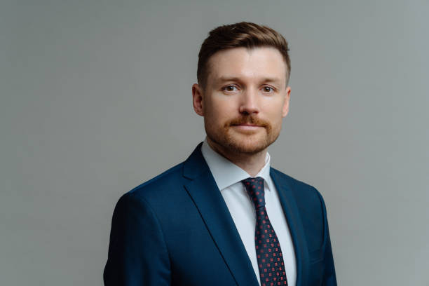 istock Handsome unshaven man in suit posing against grey background 1319015278