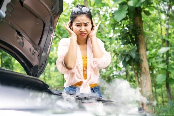 Asian woman in trouble with broken, overheat car with smoke from damaged engine Asian woman in trouble with broken, overheat car with smoke from damaged engine having problem during travel alone overheated stock pictures, royalty-free photos & images