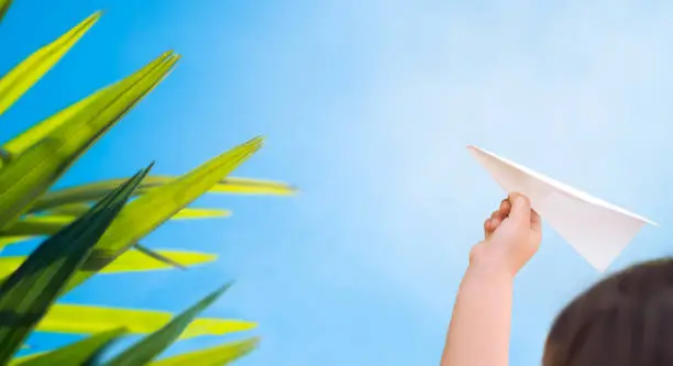 A child in his hand holds a paper plane against the background of the sky