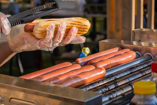 Fresh hot dog with fried sausage, served in an outdoor cafe. Cooking American barbecue food. Barbecue festival in the city park. Street fast food.