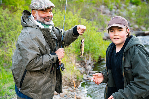 A fly fisher wearing a cervical collar and using a cane while recovering from spinal surgery. Real person. He is teaching a child how to fish.