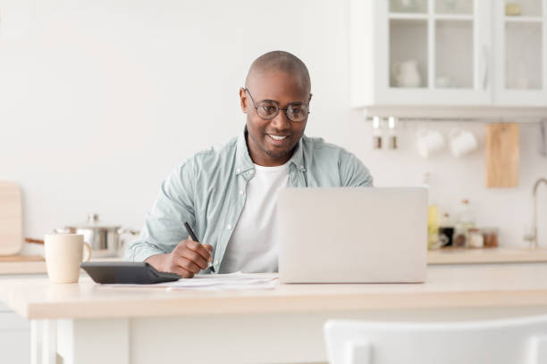 istock Plan finances. Positive african american mature man calculating taxes and using laptop computer, sitting in kitchen 1319023402
