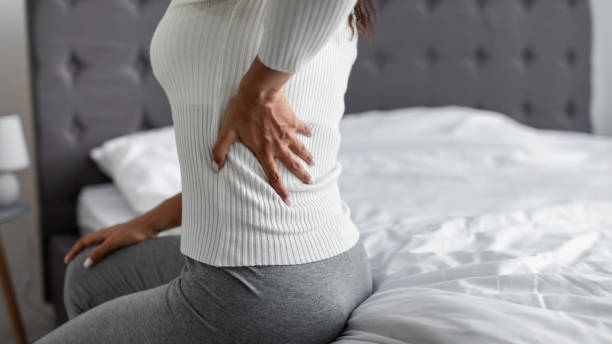 mujer con dolor de espalda lateral sentada en la cama en casa - backache pain women illness fotografías e imágenes de stock