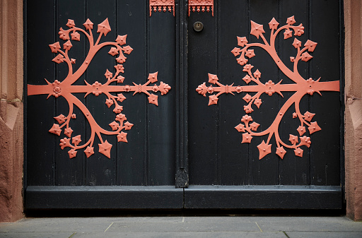 Red metal ornaments on black wooden church doors.