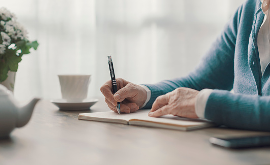 Senior woman sitting at desk and writing down notes on a notebook