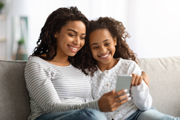 istock Cheerful african american mother and daughter using smartphone together 1319025735