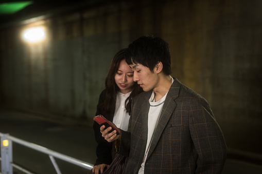 Japanese young couple talking while looking at smartphone on dark passage. Taken in Tokyo, Japan.