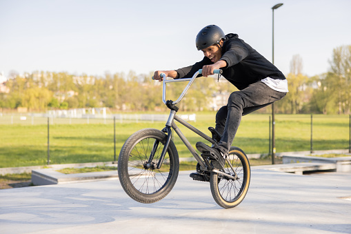 Motociclista loco monta su bicicleta baja en el skatepark, bmx levantando la rueda delantera y estando en el aire que gira su cuerpo, caderas, realiza trucos, risas, sonrisas photo