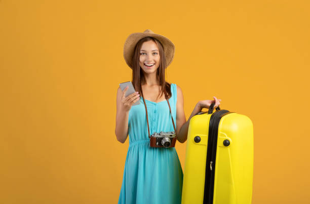 istock Happy young woman holding suitcase, using mobile phone 1319030424