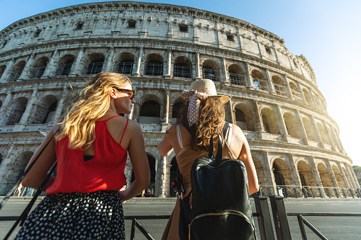 Rear view of happy young women tourists visiting italian famous landmarks at the Colosseum, Rome, Italy, Europe.