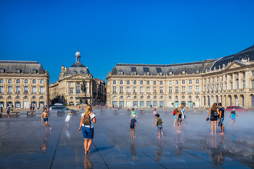 Tourists and kids having fun on the Mirroir d'eau (Water Mirror) of the Place de la Bourse in Bordeaux France on a hot summer day during a heat wave