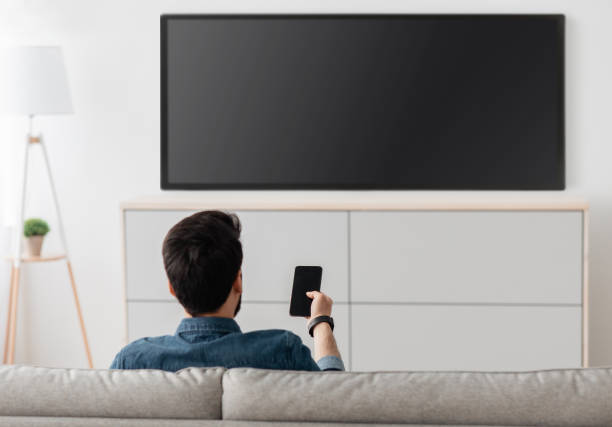 istock Modern gadgets. Unrecognizable man with smartphone connected to TV, watching video at home, back view 1319037522