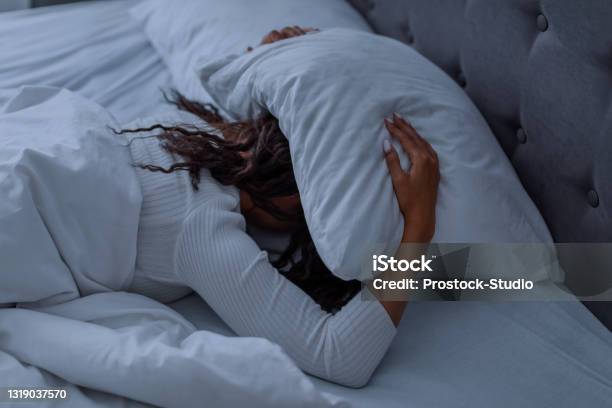 Stressed Black Woman Covering Head Under Pillow Lying In Bed Stock Photo - Download Image Now